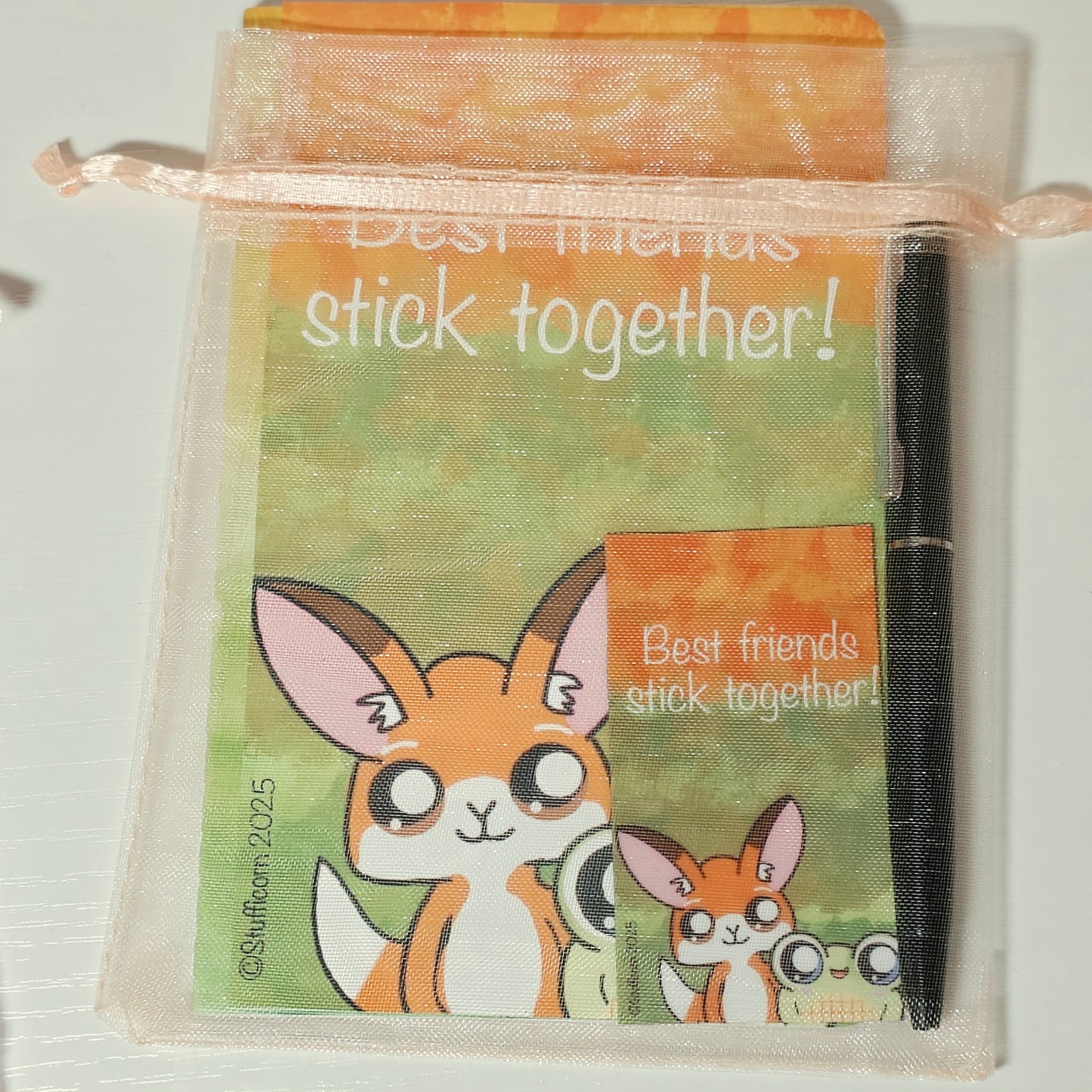 Small notepad with Jo the Fox and Luci the frog on the cover. Mini pen and magnet included inside a peach mesh bag with peach ribbon