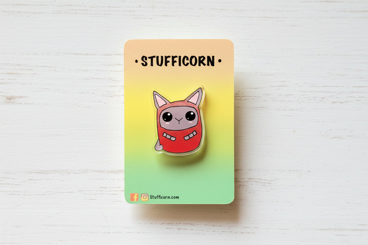 an acrylic pin of a grey cat in a red daruma outfit