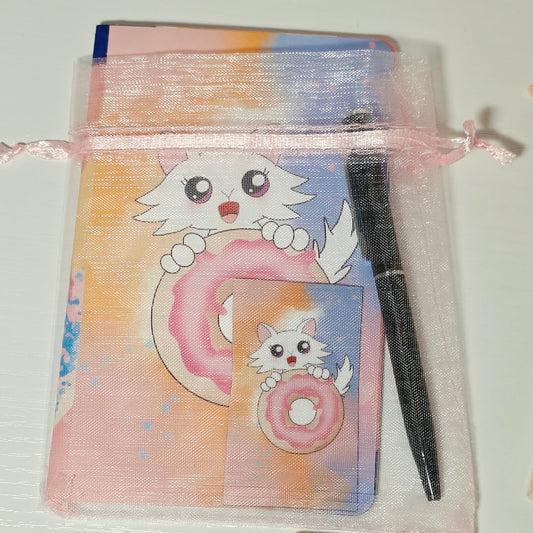 Small notepad with Daisy the Cat holding a donut on the cover. Mini pen and magnet included inside a pink mesh bag with pink ribbon