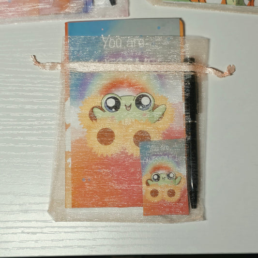 Small notepad with a colorful cover featuring a frog character, mesh bag held open by a ribbon